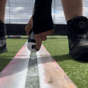 A person using a 6 Pack of White Soppec Artificial Surface Marking Aerosols to mark lines on artificial turf.