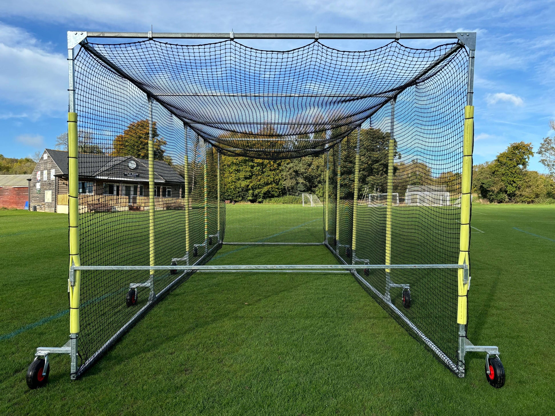 11m Anti-Vermin Mobile Batting Cage on a grass field with clear sky and background buildings.