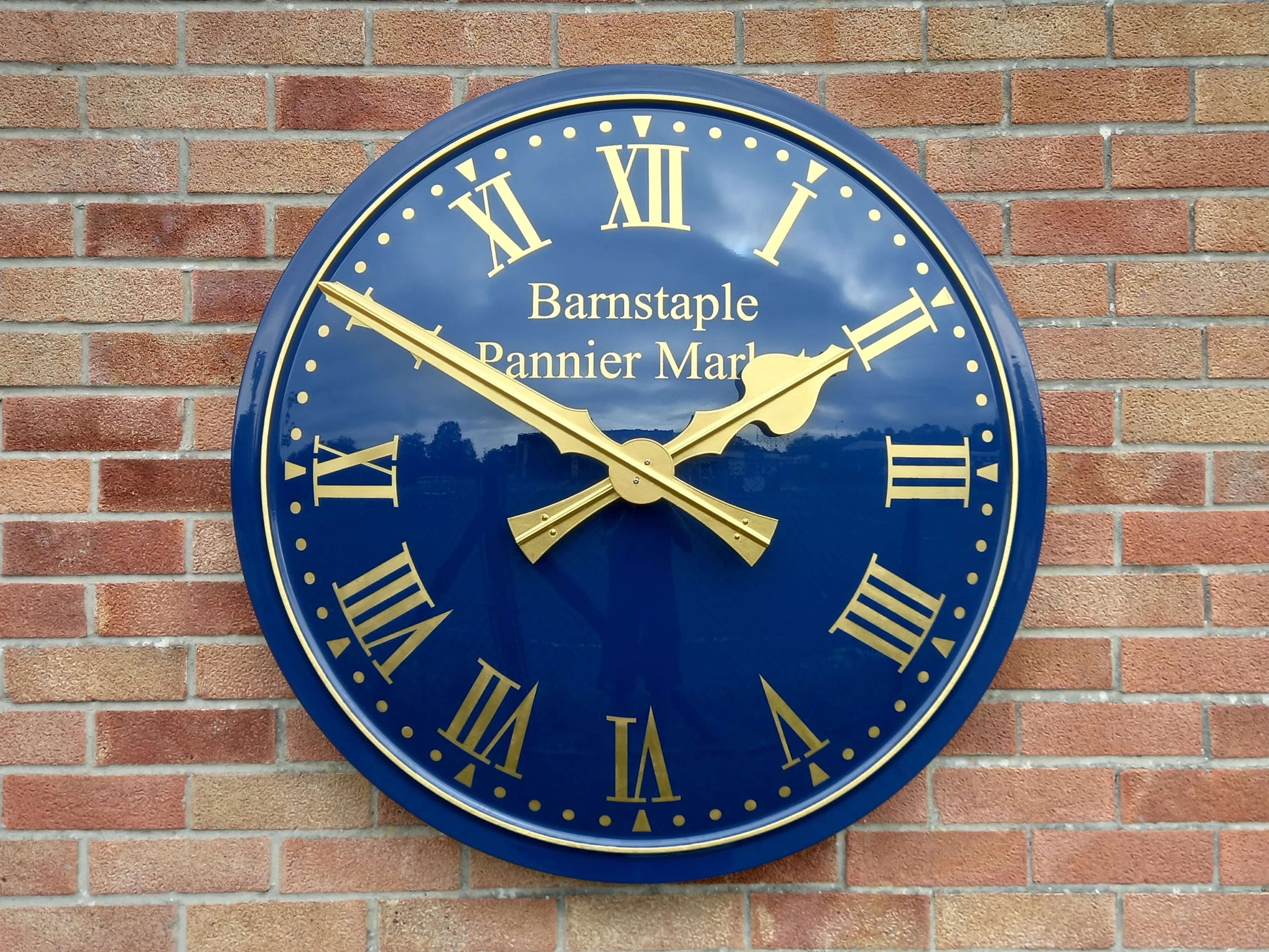 Cricket Pavilion Clocks on a wall with a blue dial and gold hands, showcasing a traditional design.