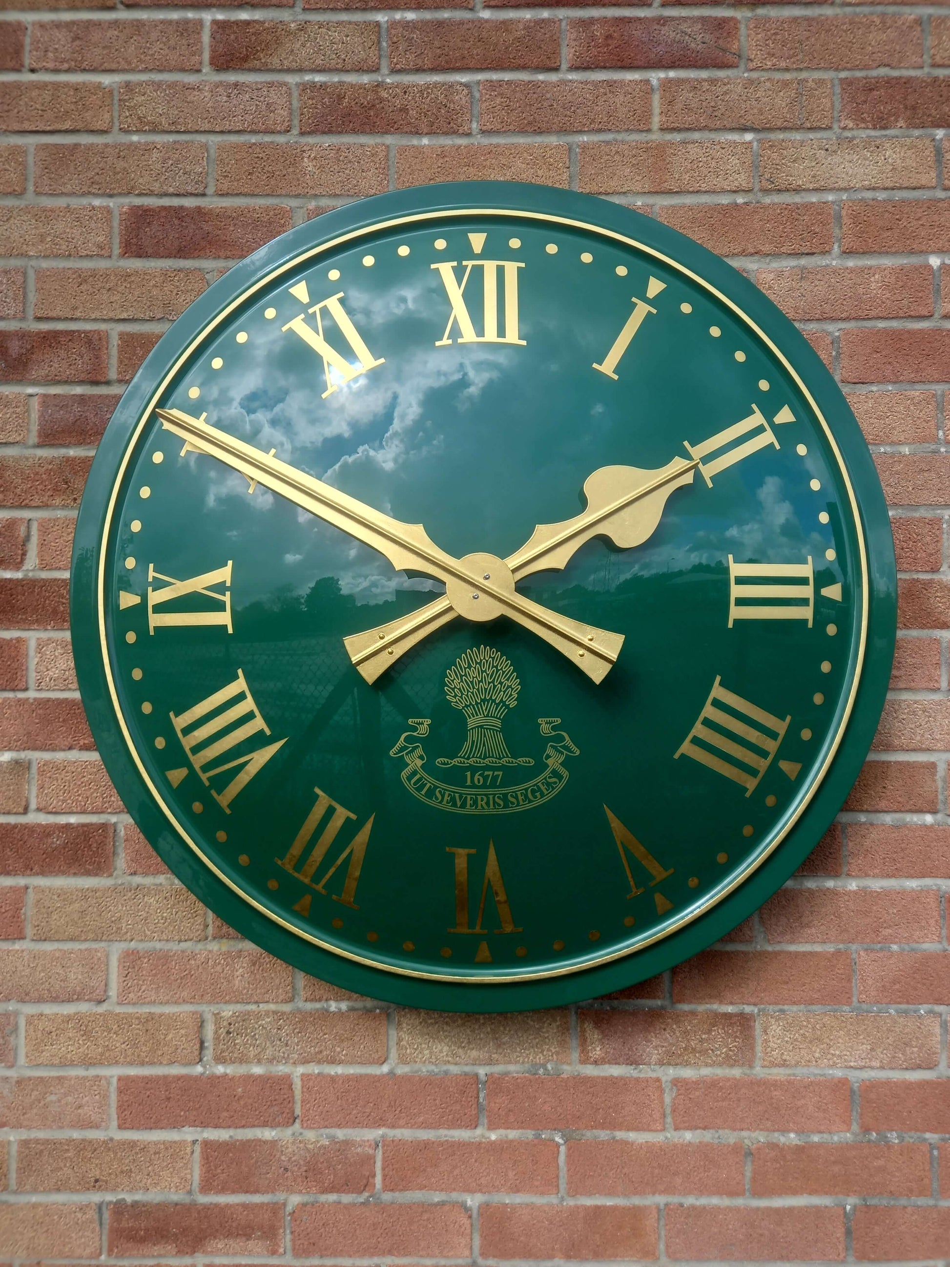 Cricket Pavilion Clocks with gold hands on a green background mounted on a brick wall.