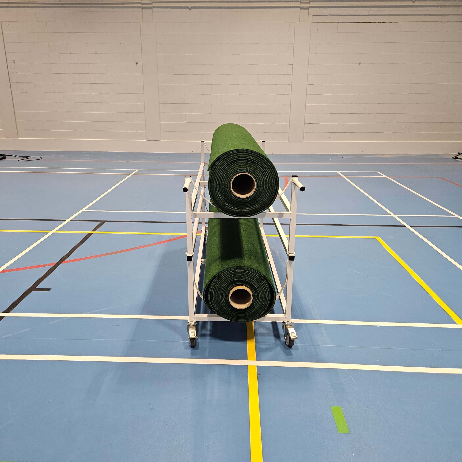 Piggy Back Carpet Trolley holding two rolls of green carpet mats on a sleek blue gym floor.