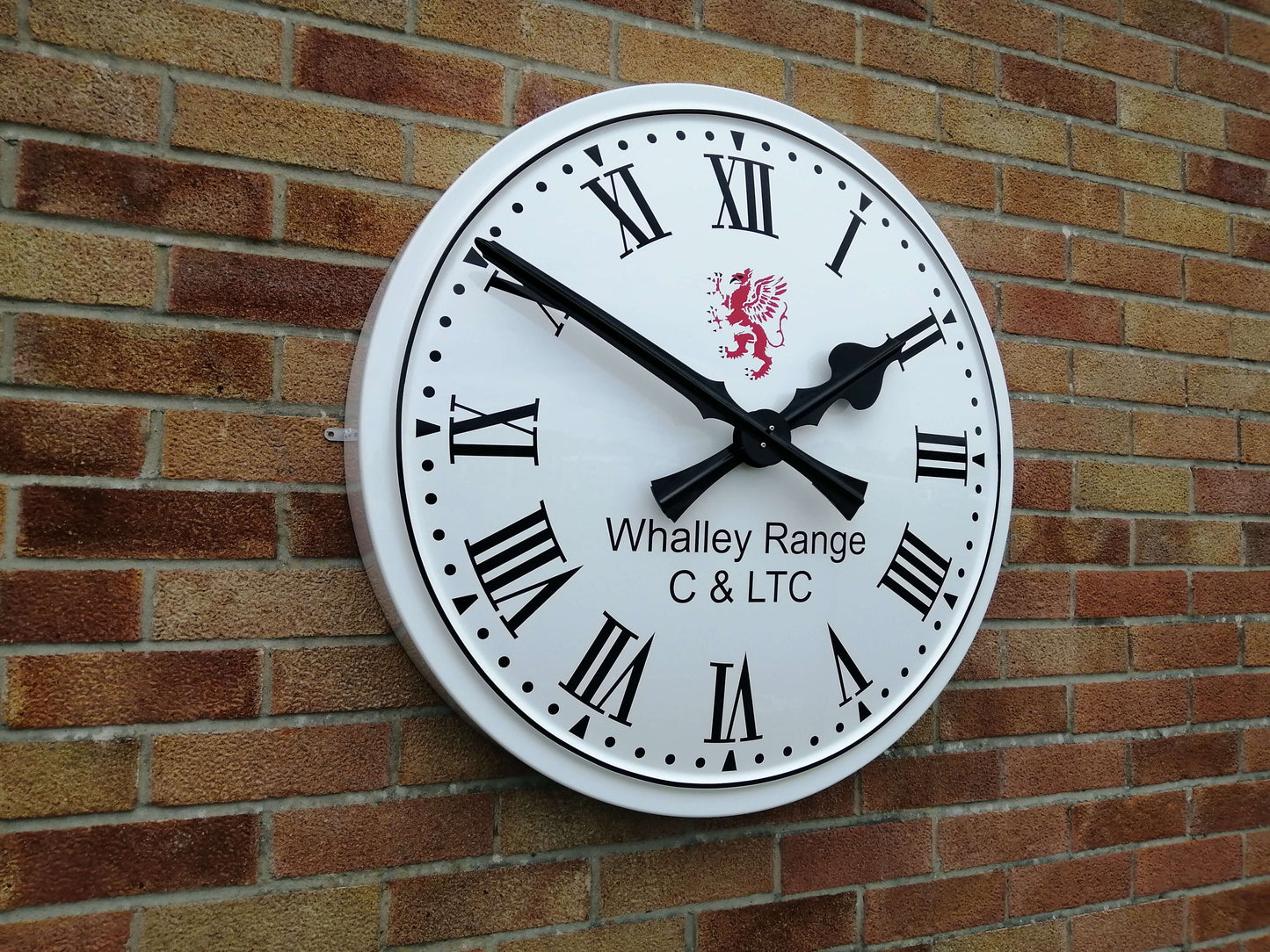 Cricket Pavilion Clocks on a brick wall with Roman numerals and a decorative lion design.